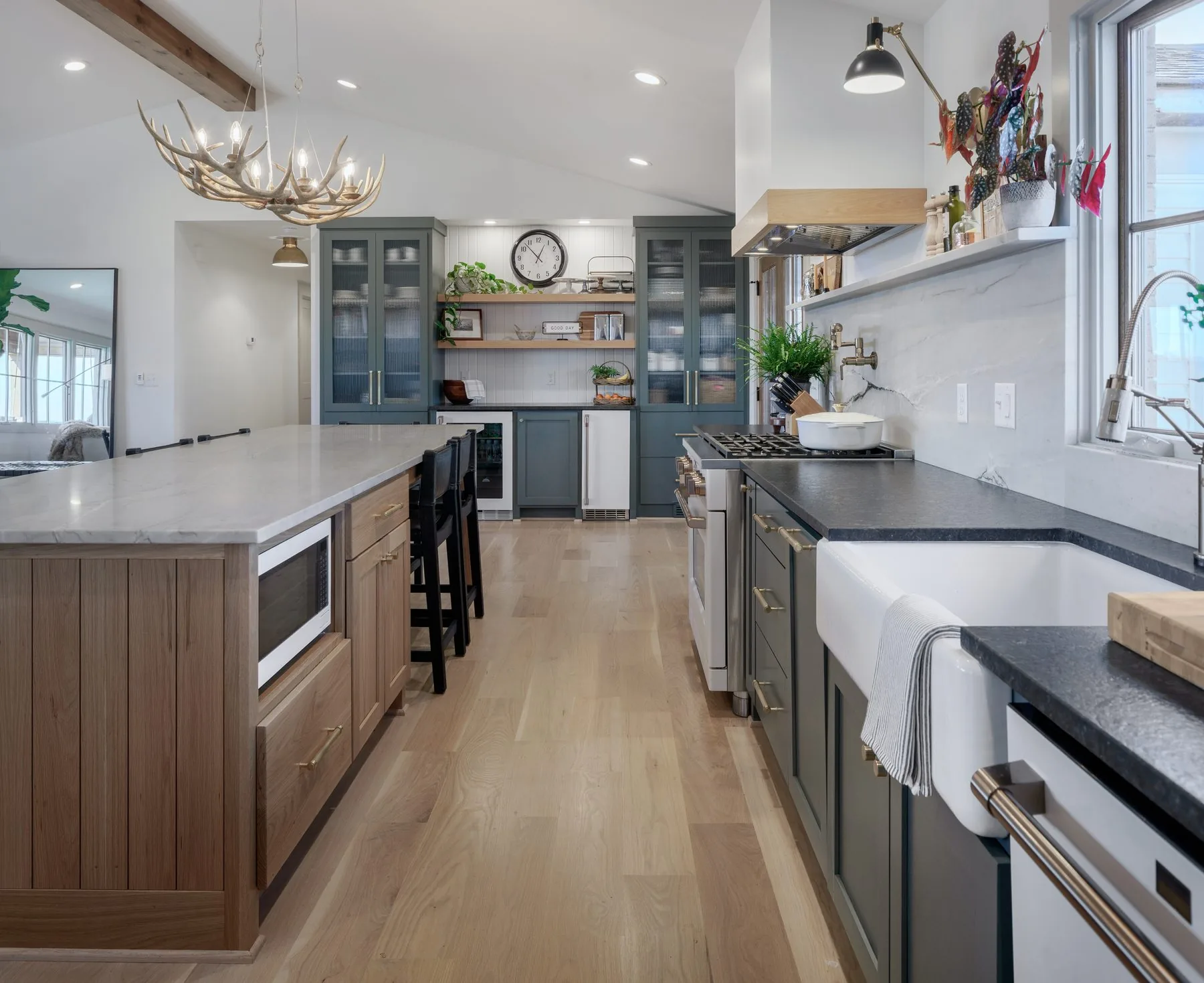 Kitchen with deep green upper cabinets, white oak lower cabinetry and a marble island