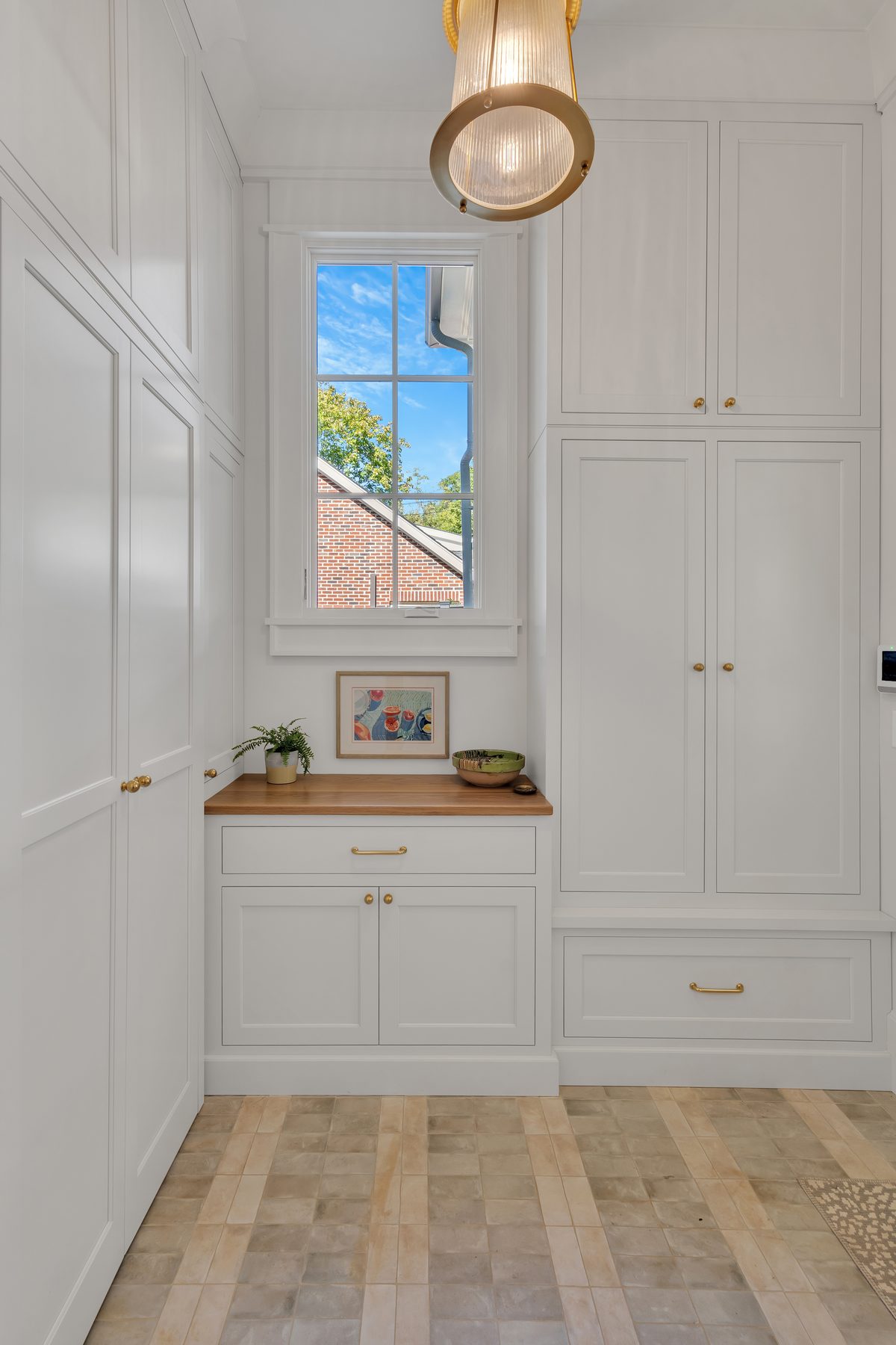 White mudroom cabinetry with a wood counter under a window