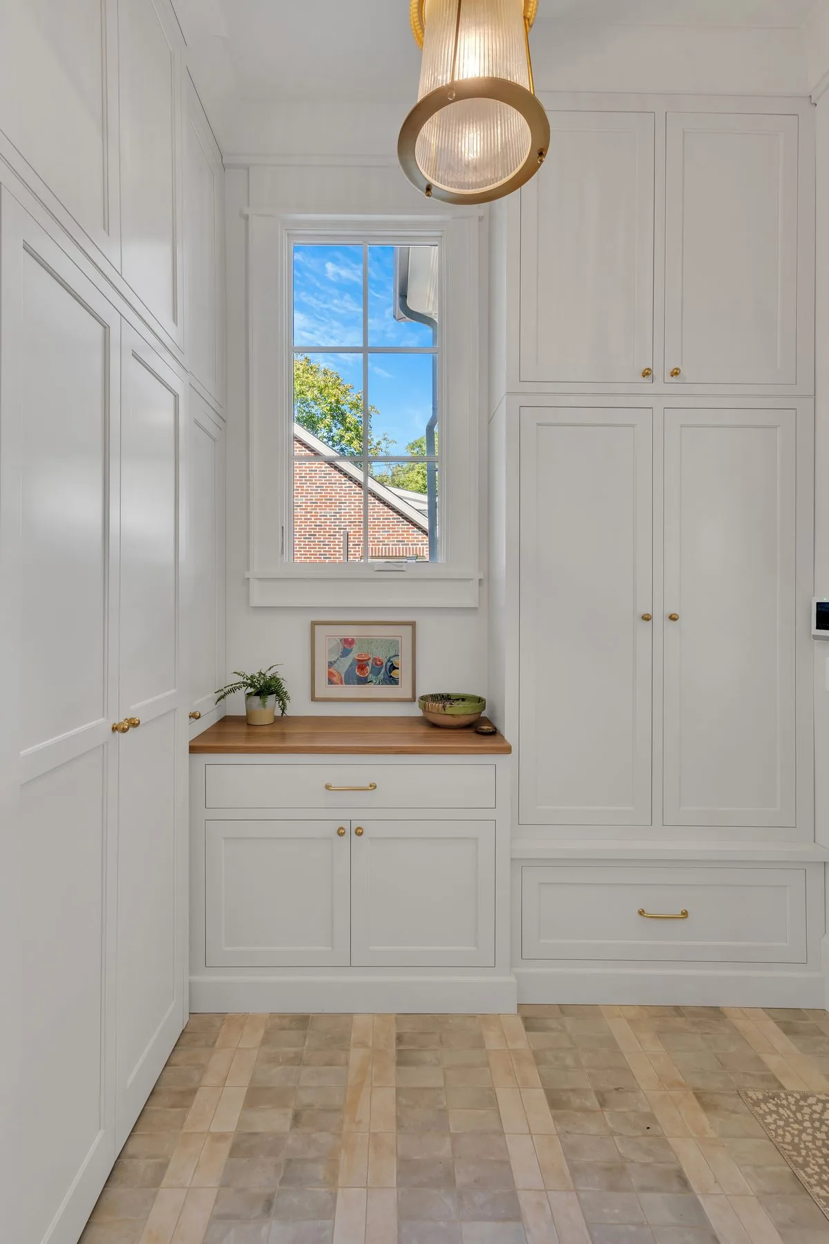 White mudroom cabinetry with a wood counter under a window